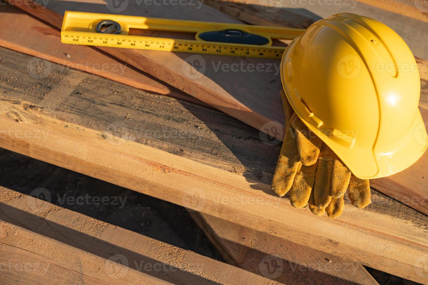 resumen de la construcción de cascos, guantes y nivel descansando sobre tablones de madera foto