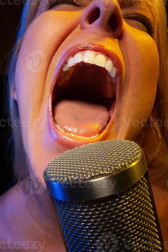 Female vocalist under gelled lighting sings with passion into condenser microphone. photo