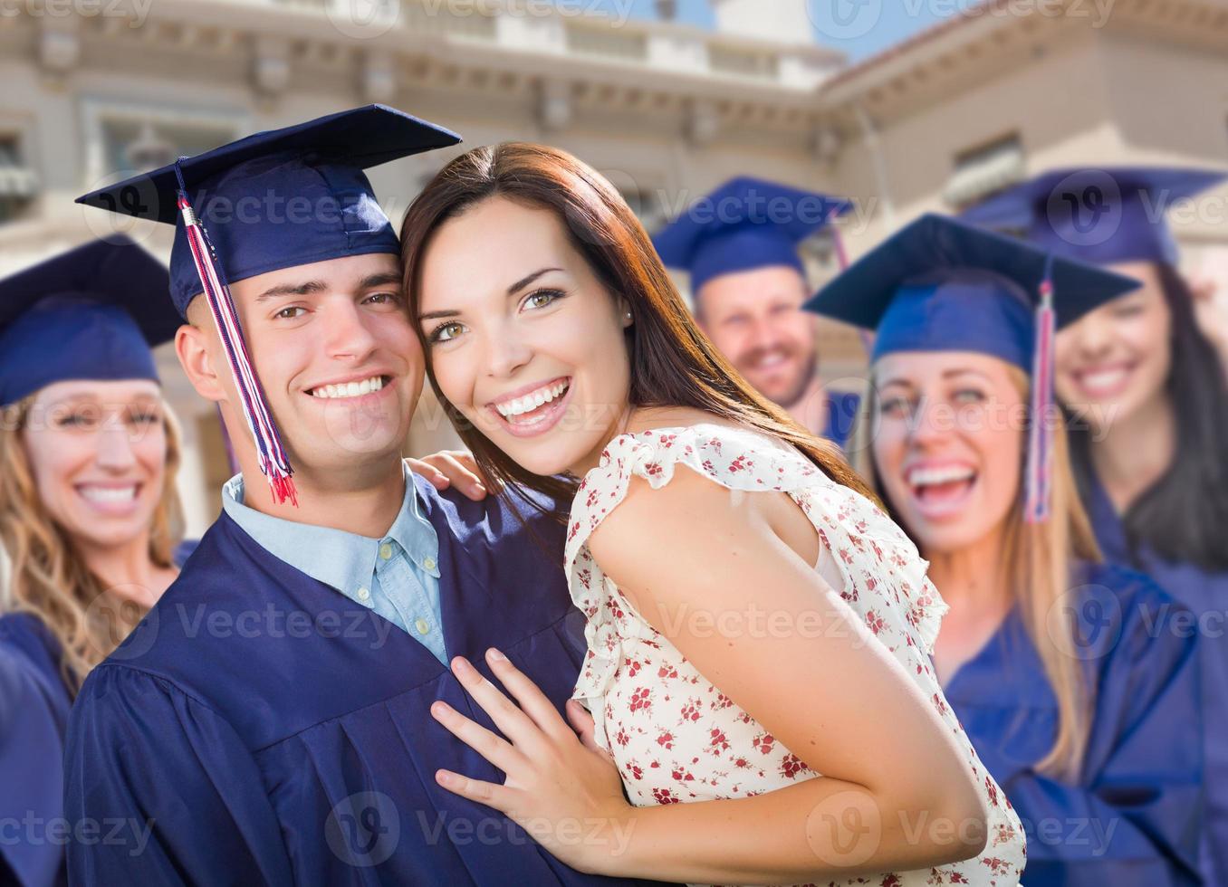 orgulloso graduado masculino en toga y birrete con una chica entre otros graduados detrás foto