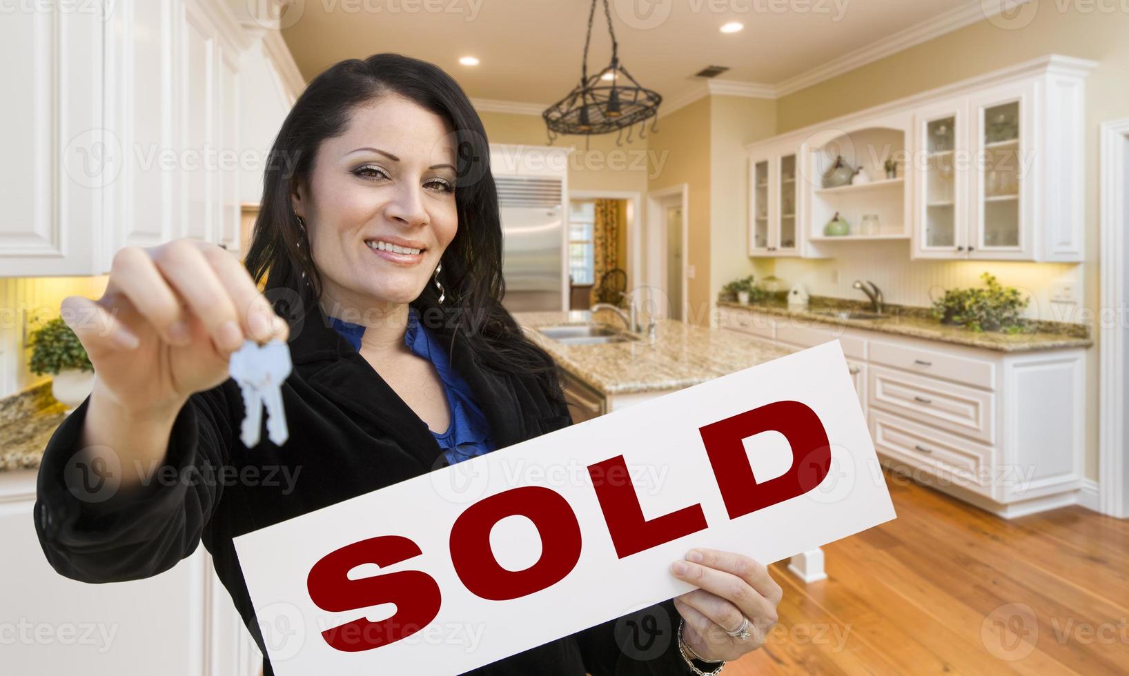 Hispanic Woman In Kitchen Holding House Keys and Sold Sign photo