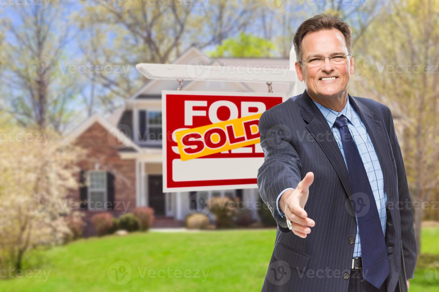 Male Agent Reaching for Hand Shake in Front of House and Sold Real Estate Sign photo