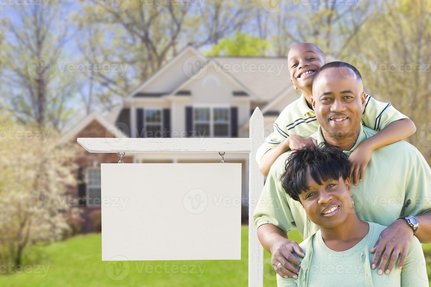 familia afroamericana frente a una casa y un cartel de bienes raíces en blanco foto