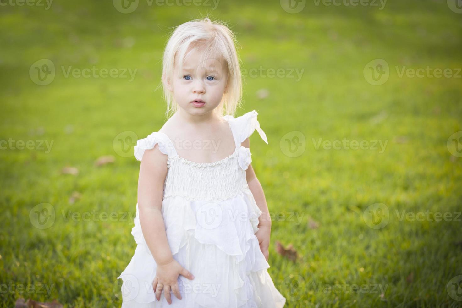 Adorable Little Girl Wearing White Dress In A Grass Field photo