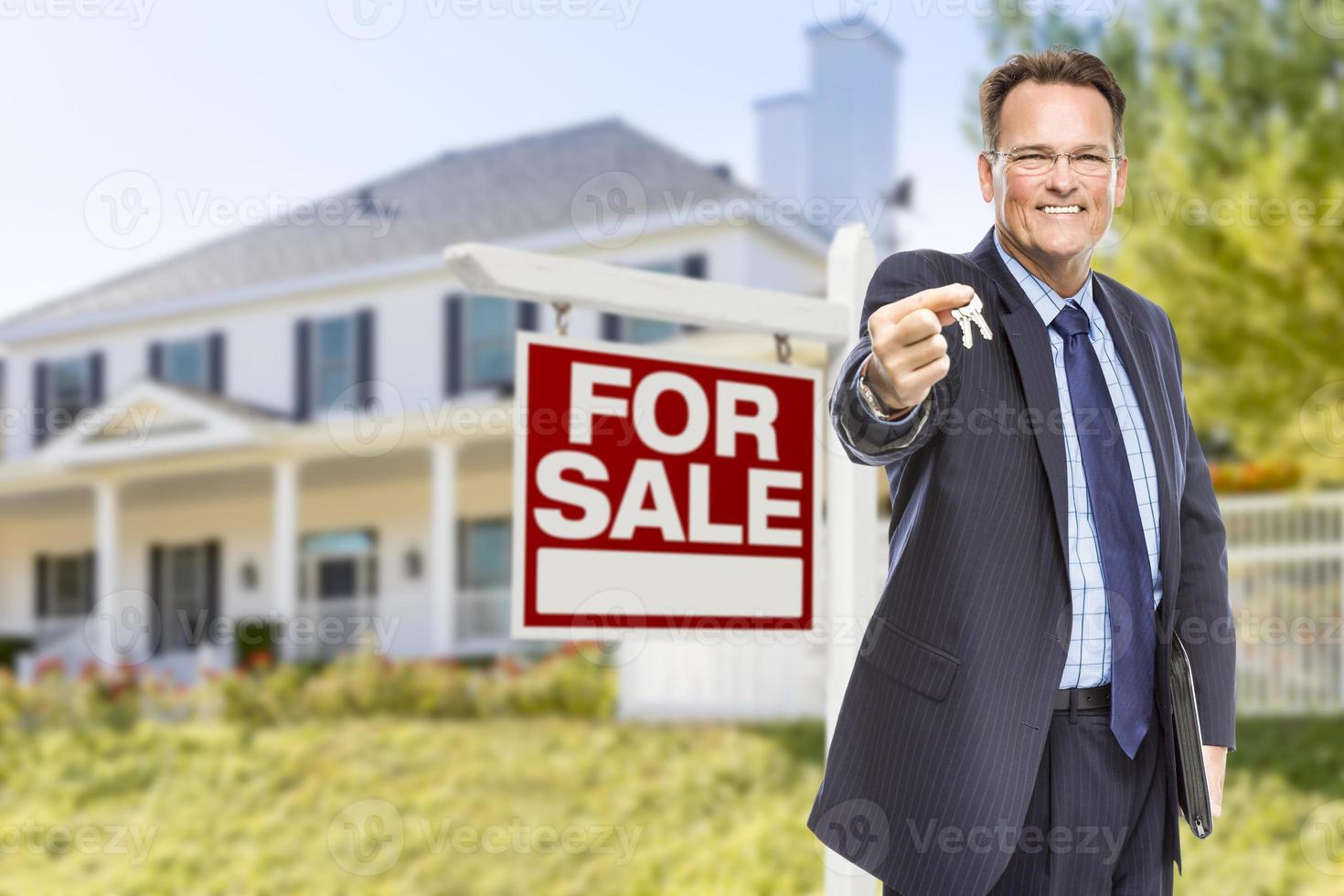agente con llaves frente al letrero de venta y la casa foto