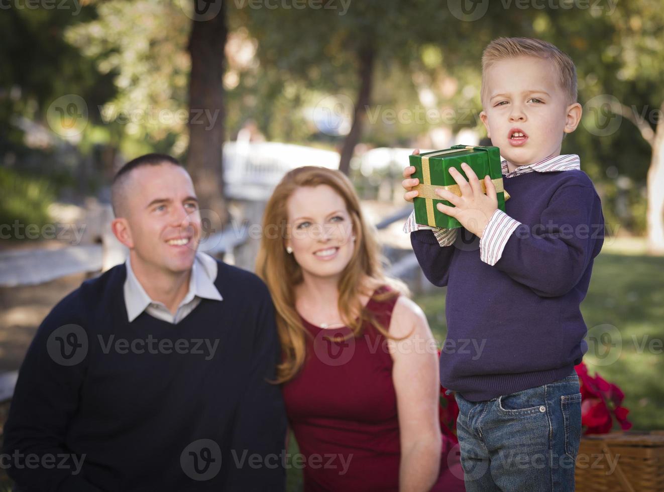 niño sosteniendo un regalo de navidad en el parque mientras los padres miran foto