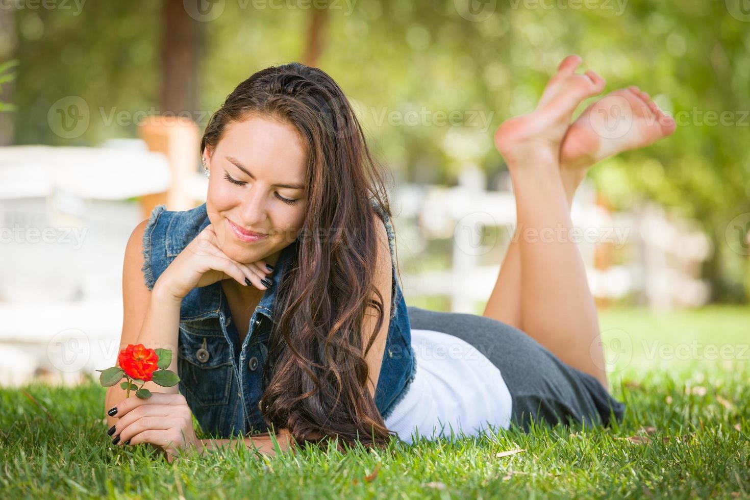 Attractive Mixed Race Girl Portrait Laying in Grass Outdoors with Flower. photo