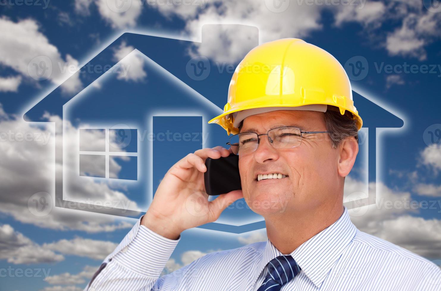 Contractor in Hardhat on Phone Over House Icon and Blurry Clouds photo