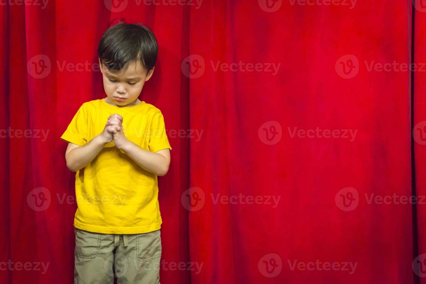 Mixed Race Boy Praying in Front of Red Curtain photo