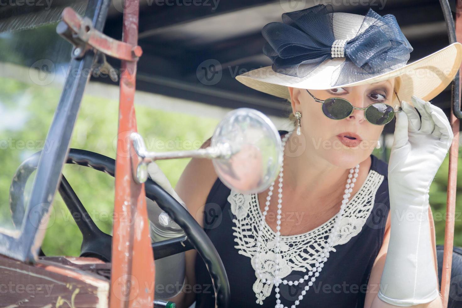 Attractive Woman in Twenties Outfit Checking Makeup in Antique Automobile photo