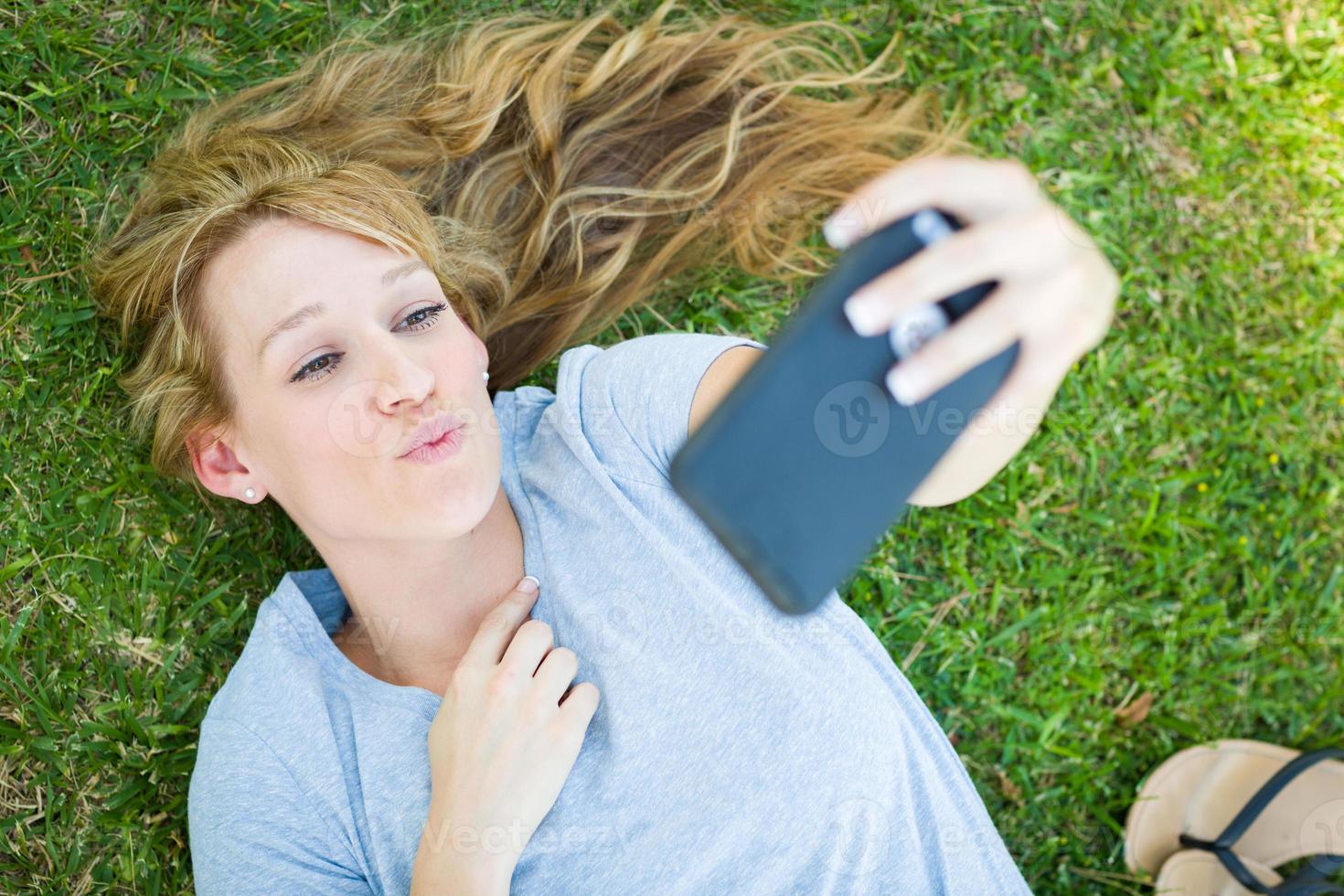 Young Adult Woman Laying in Grass Taking a Selfie with Her Smart Phone. photo