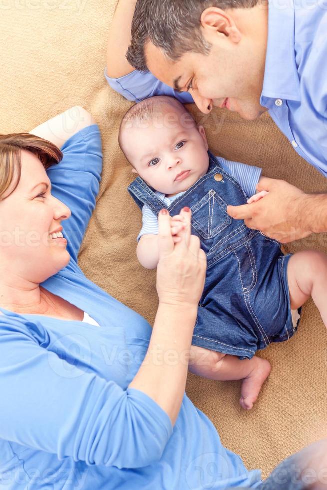 Young Mixed Race Couple Laying With Their Infant On A Blanket photo