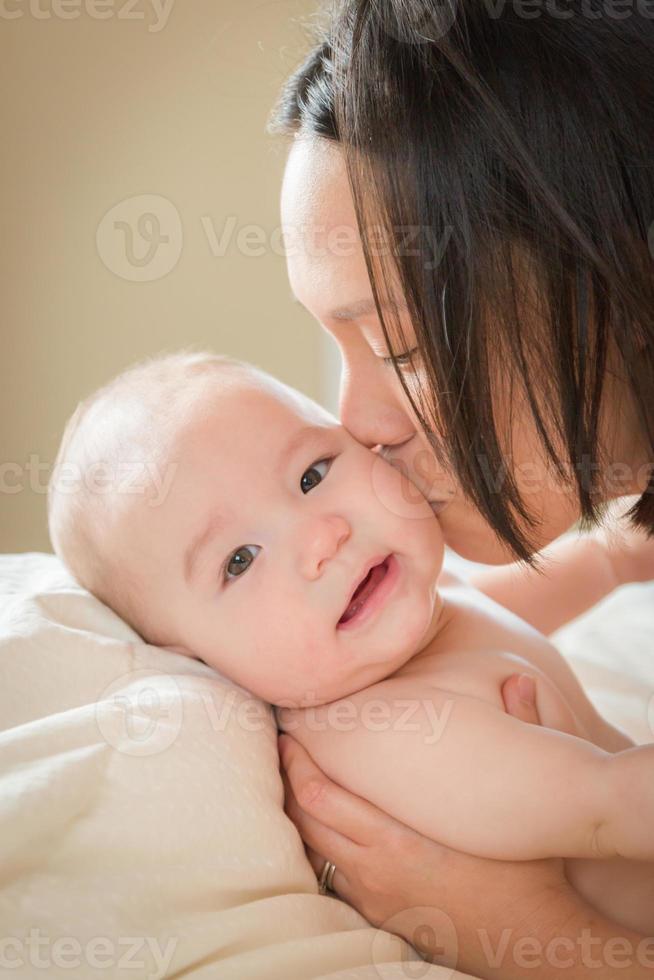 Bebé chino y caucásico de raza mixta acostado en la cama con su madre foto