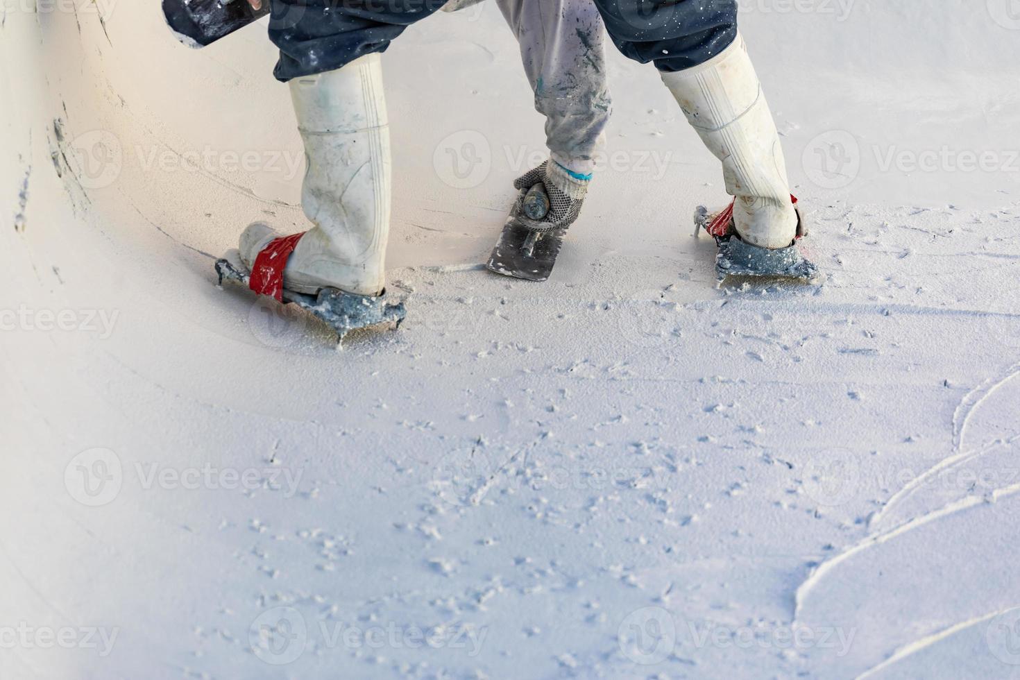 trabajador que usa zapatos con púas alisando el yeso húmedo de la piscina con una paleta foto