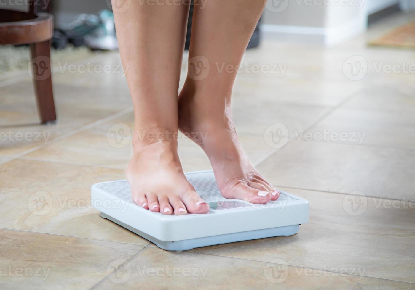 Woman Standing on Weight Scale At Home photo