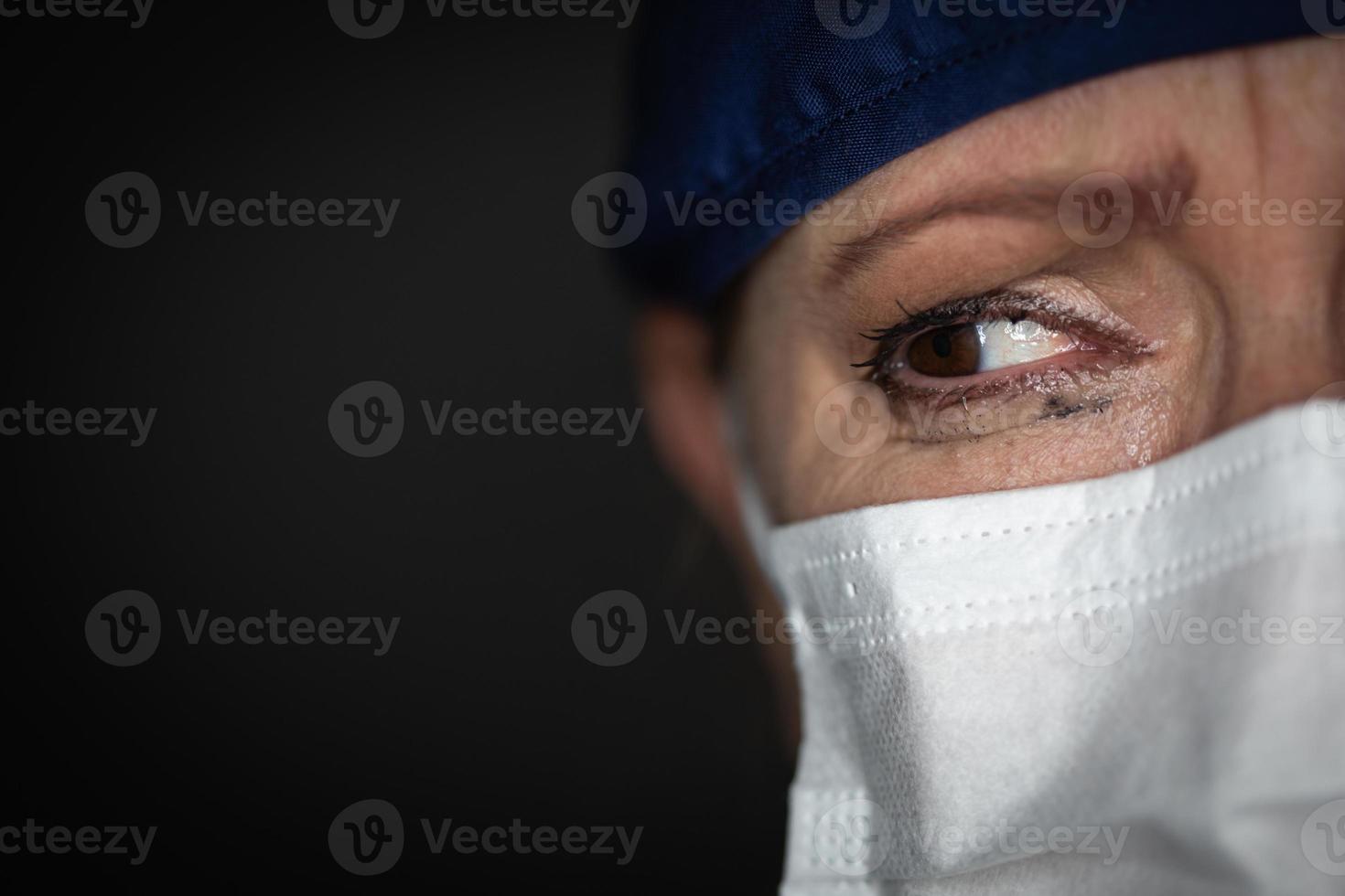 Tearful Stressed Female Doctor or Nurse Wearing Medical Face Mask on Dark Background photo