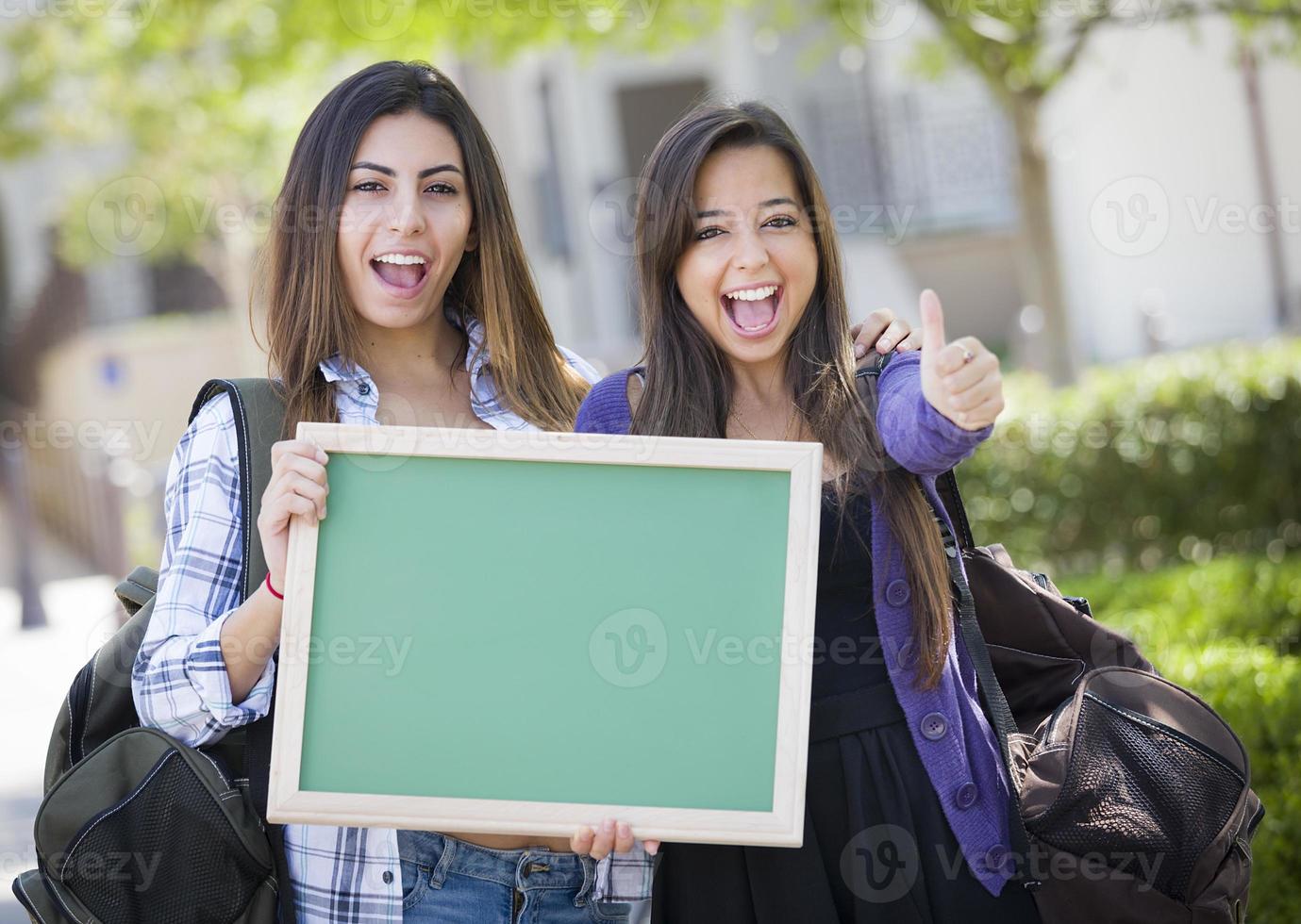 Mixed Race Female Students with Thumbs Up Holding Blank Chalkboard photo