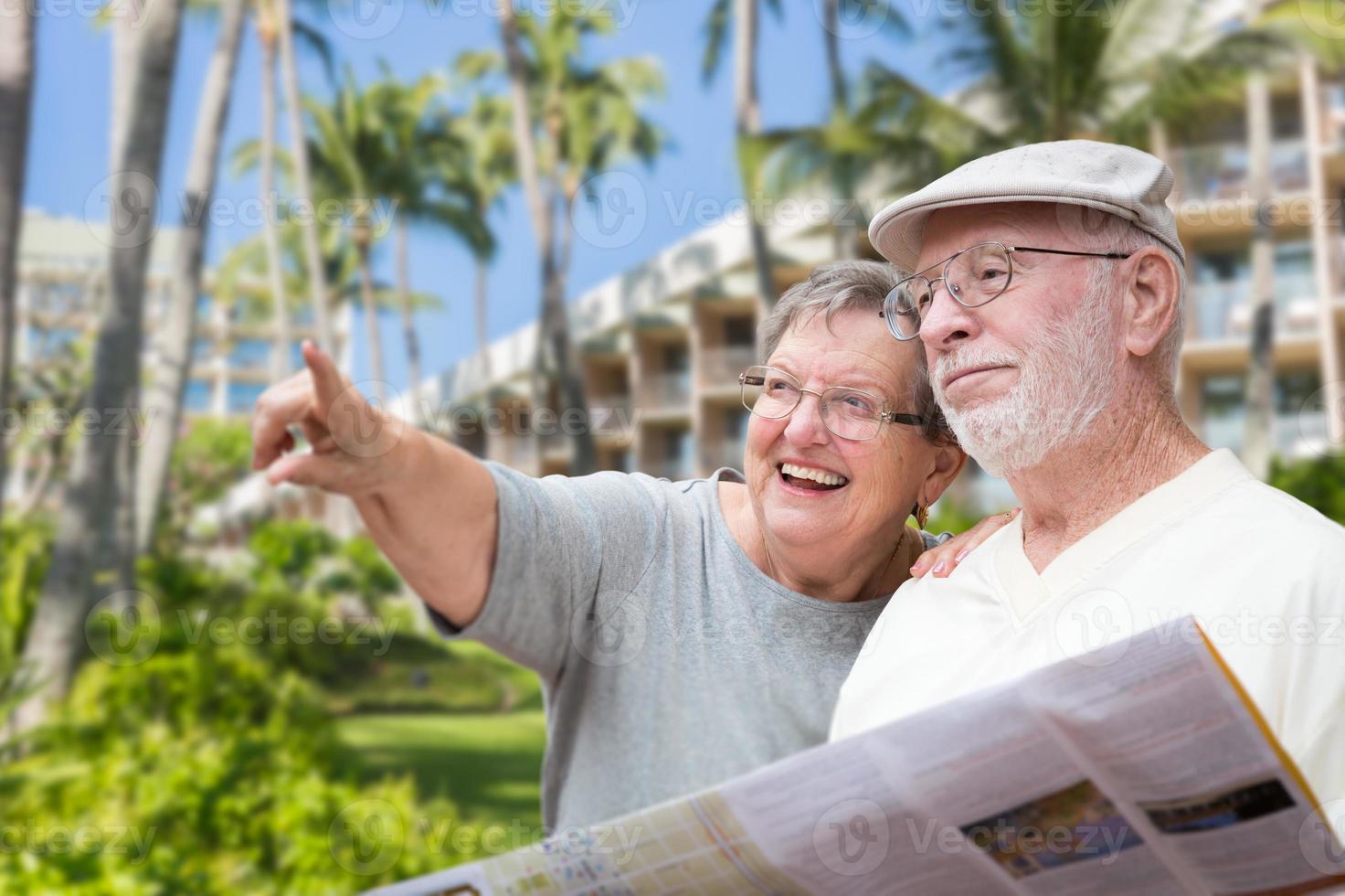 feliz pareja de adultos mayores turistas con folleto junto al hotel tropical y palmeras. foto