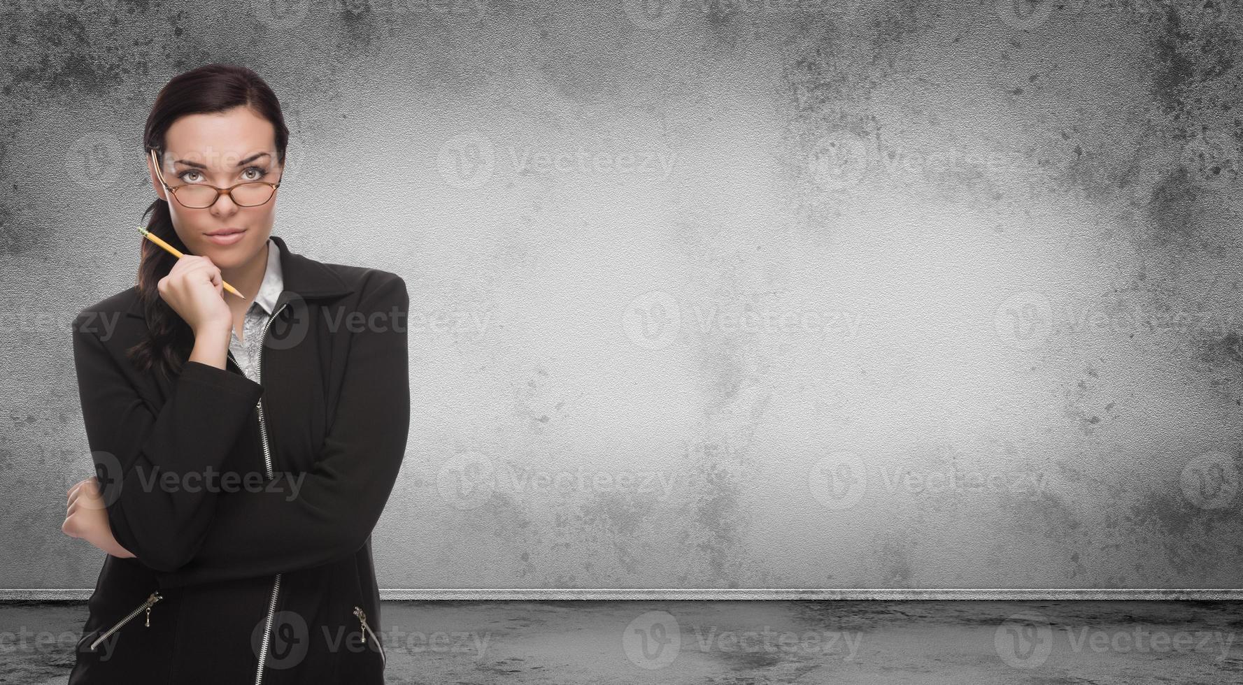 mujer adulta joven con lápiz y anteojos de pie frente a una pared en blanco grungy en blanco con espacio de copia foto