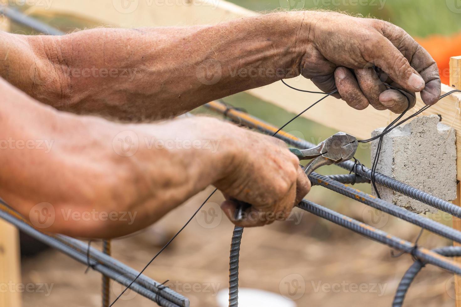 Trabajador que asegura la estructura de barras de refuerzo de acero con la herramienta de corte de alicates de alambre en el sitio de construcción foto