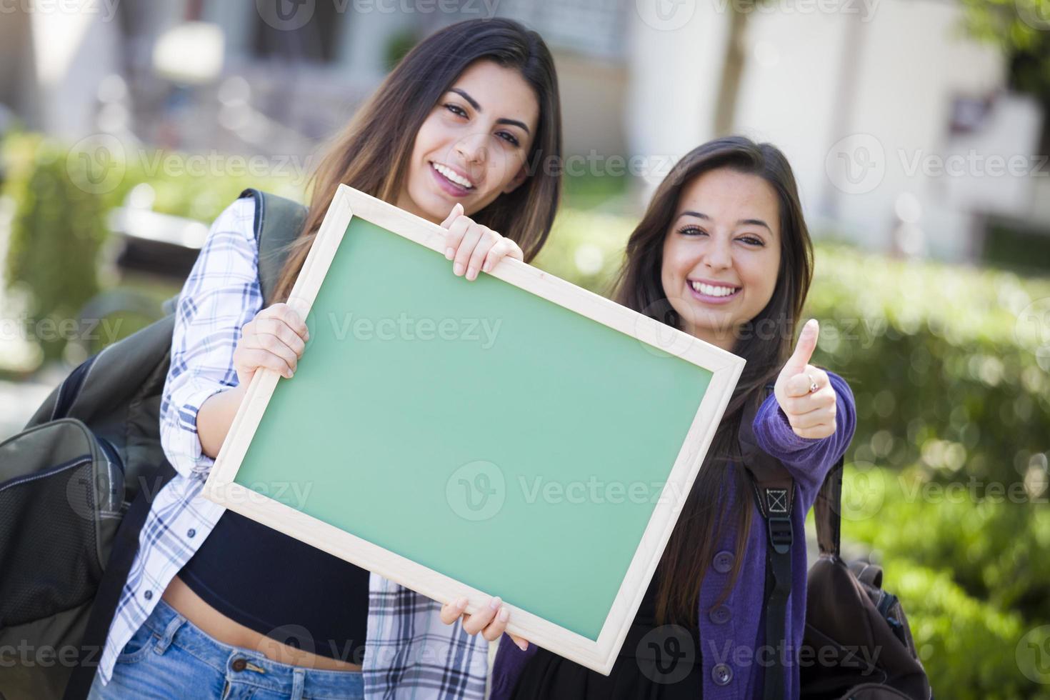 Mixed Race Female Students with Thumbs Up Holding Blank Chalkboard photo