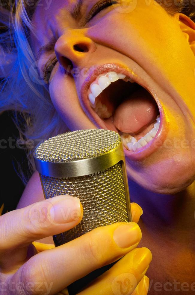 Female vocalist under gelled lighting sings with passion into condenser microphone. photo