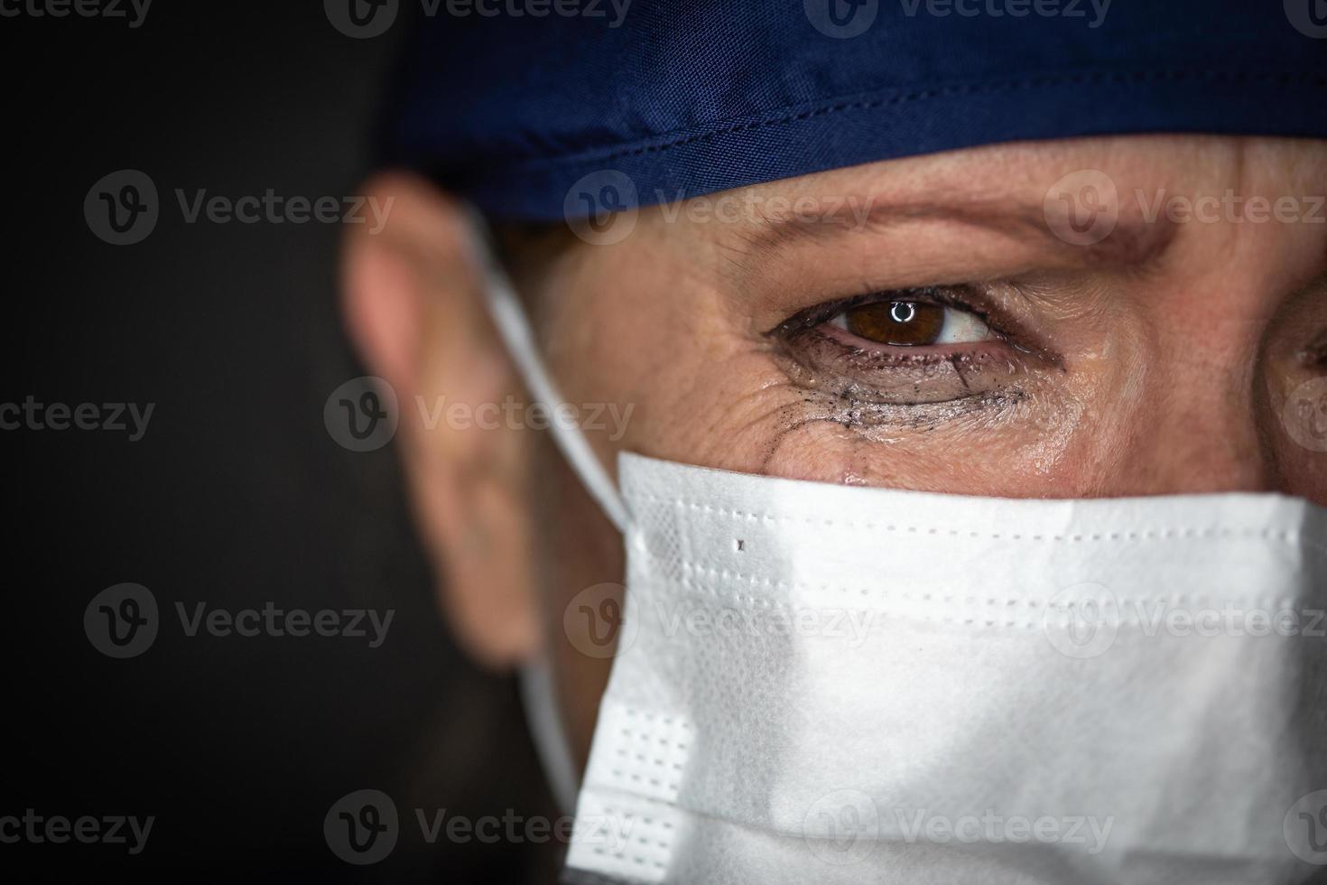 Tearful Stressed Female Doctor or Nurse Wearing Medical Face Mask on Dark Background photo