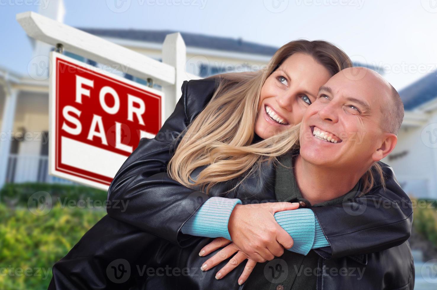 Happy Couple Hugging in Front of For Sale Real Estate Sign and House photo