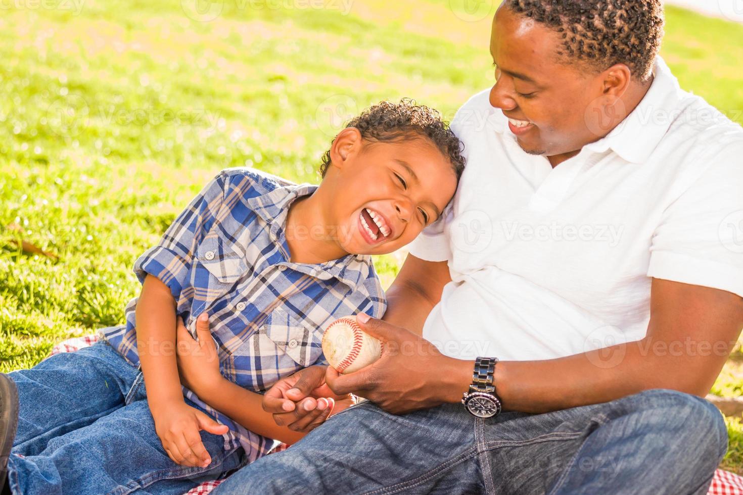 padre afroamericano e hijo de raza mixta jugando con béisbol en el parque foto