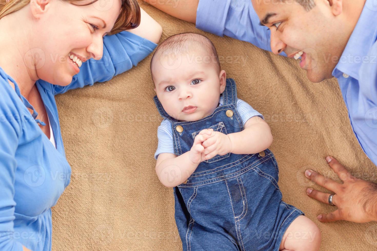 joven pareja de raza mixta acostada con su bebé en una manta foto