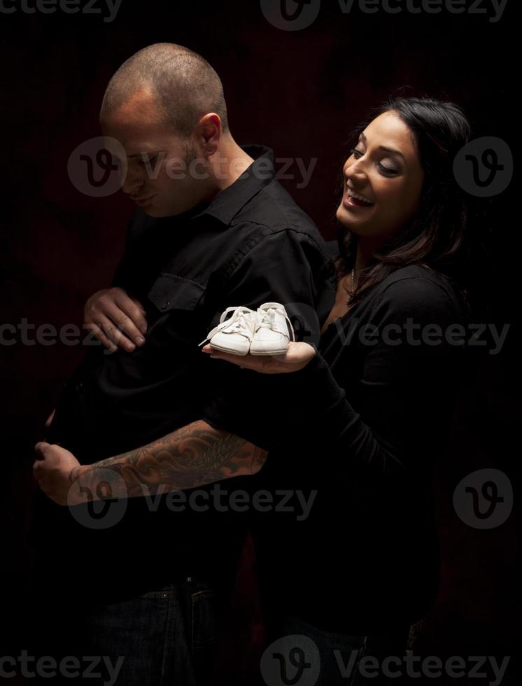 Mixed Race Couple Holding New White Baby Shoes on Black photo
