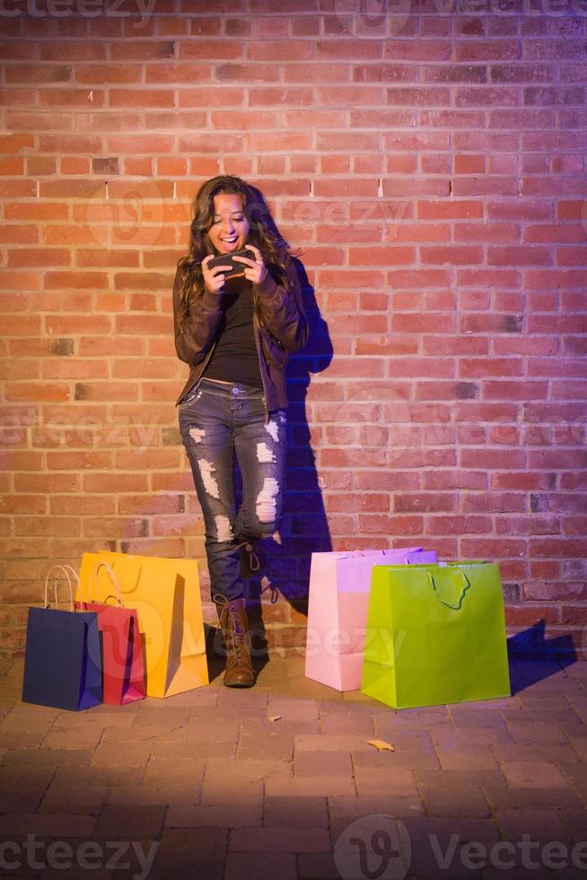 Woman with Shopping Bags Using Cell Phone Against Brick Wall photo