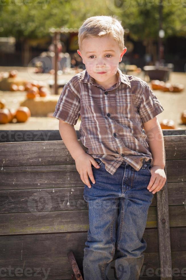 niño pequeño con las manos en los bolsillos en el huerto de calabazas foto