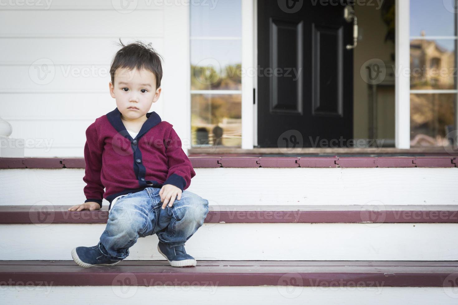 Melancholy Mixed Race Boy Sitting on Front Porch Steps photo