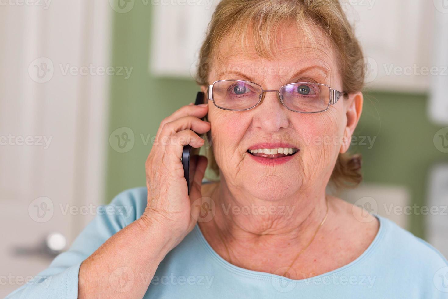 Happy Senior Adult Woman on Her Smart Cell Phone in Kitchen photo