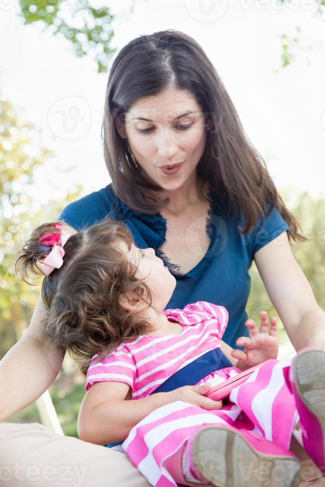 Mixed Race Mother and Cute Baby Daughter Playing with Cell Phone in Park. photo