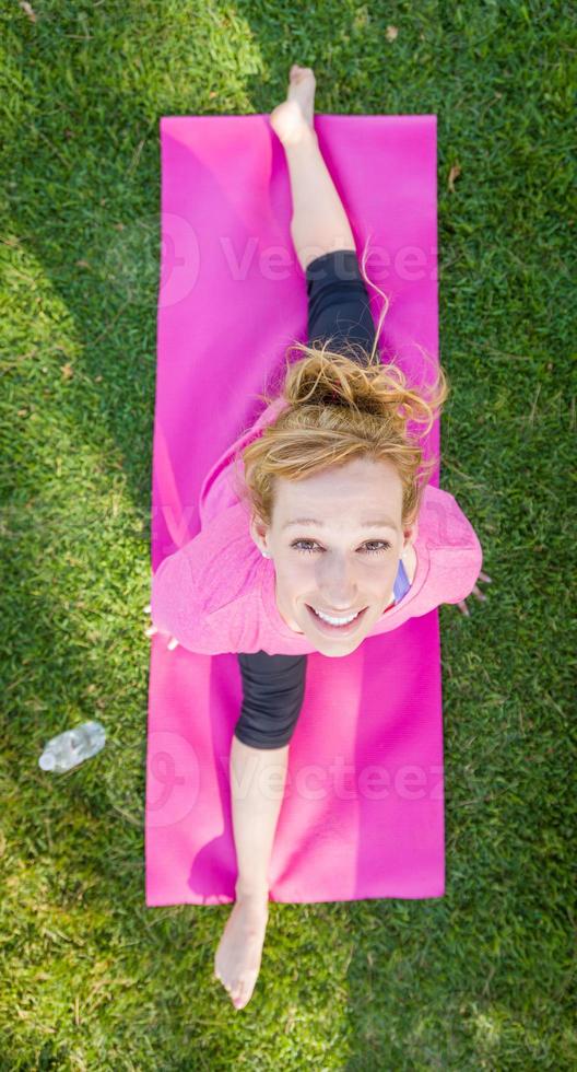 Overhead of Young Fit Flexible Adult Woman Outdoors on The Grass With Yoga Mat Doing The Splits. photo