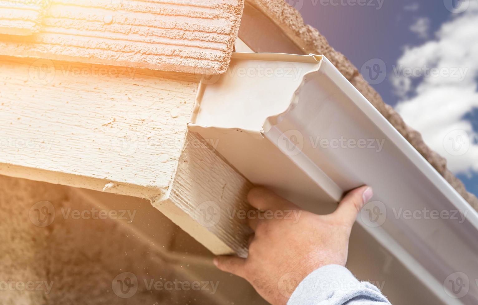 Worker Attaching Aluminum Rain Gutter to Fascia of House photo