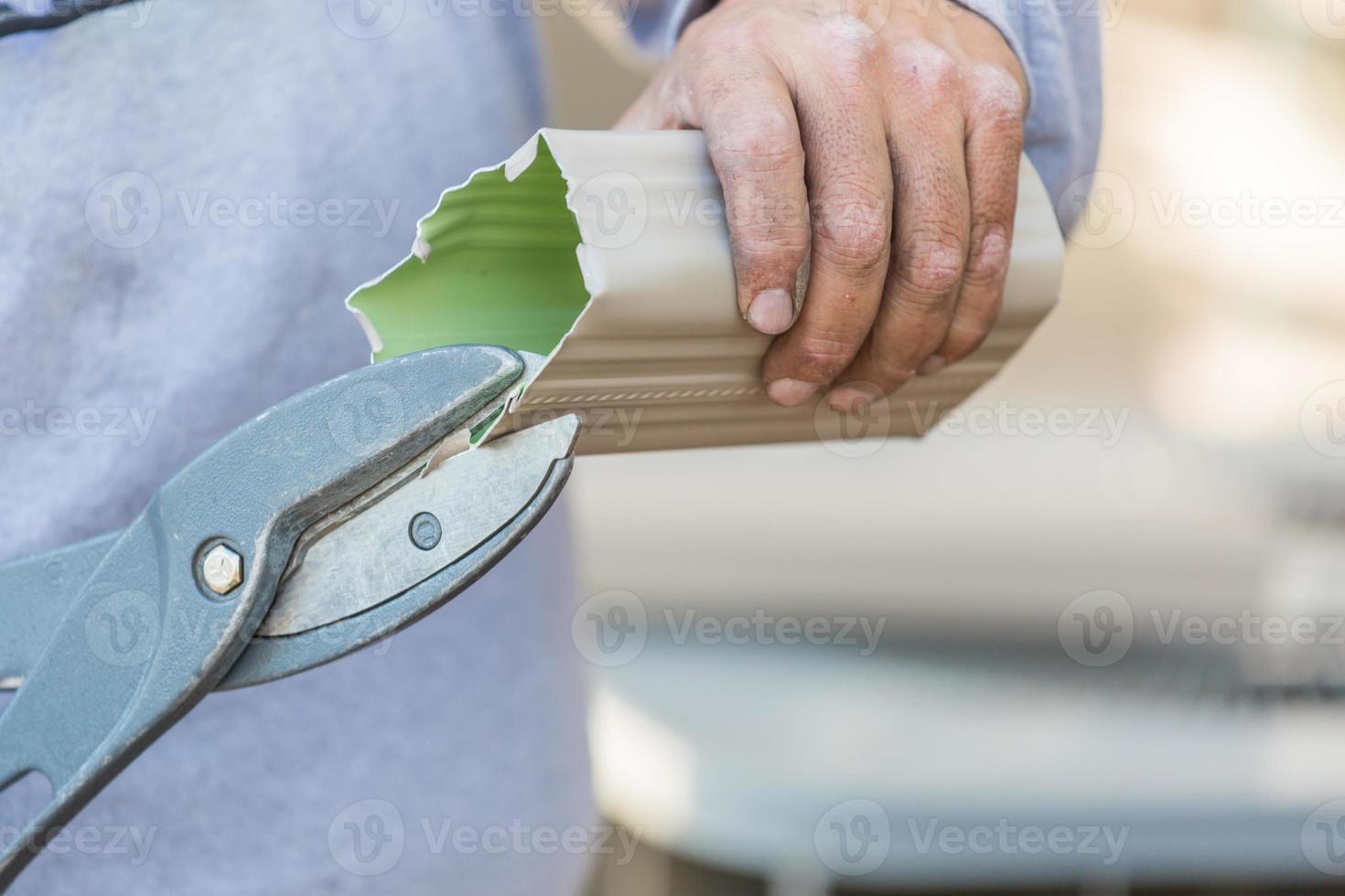 Worker Cutting Aluminum Rain Gutter With Heavy Shears. photo