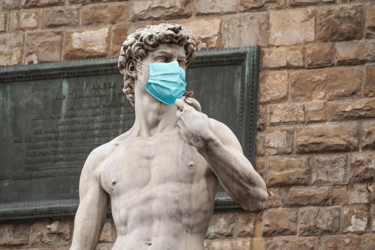 The Statue Of David in the Piazza della Signoria In Italy Wearing Blue Protective Medical Face Mask photo