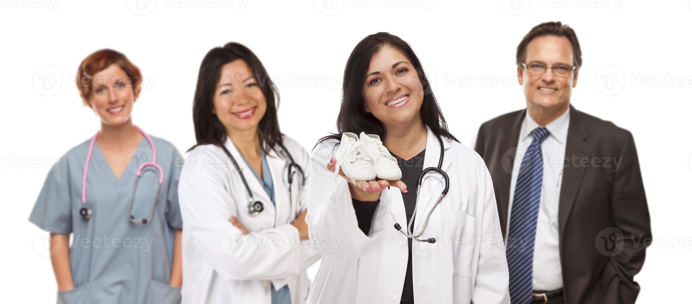 Hispanic Female Doctor or Nurse with Baby Shoes and Support Staff Behind photo