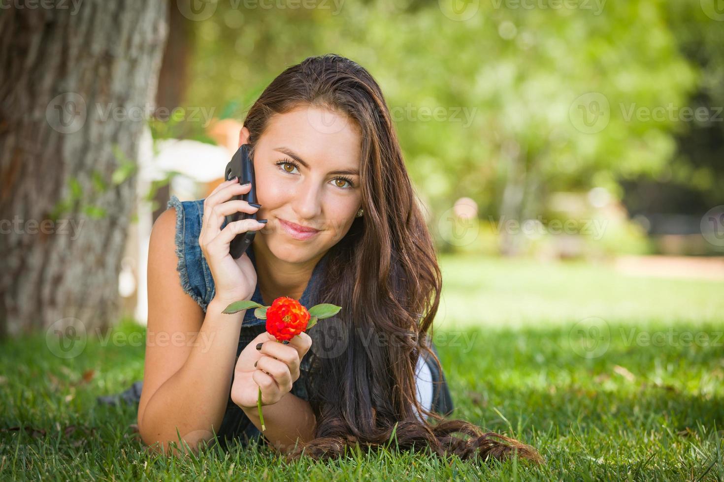 Attractive Happy Mixed Race Young Female Talking on Cell Phone Outside Laying in the Grass photo