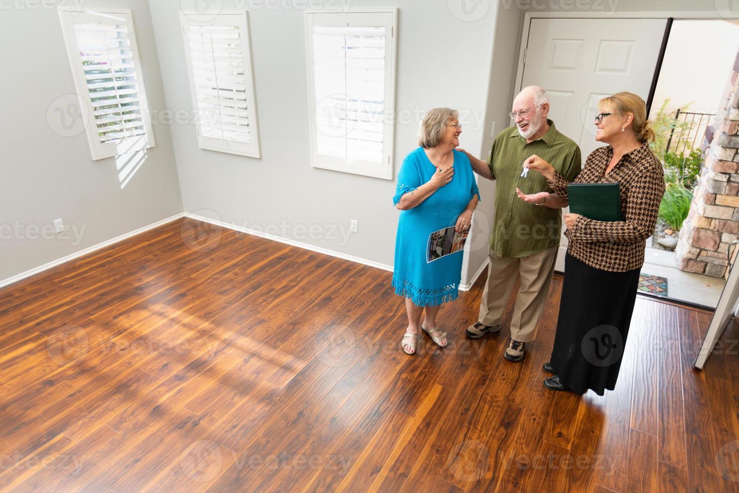 Female Real Estate Agent Handing New House Keys to Senior Adult Couple In New Home photo