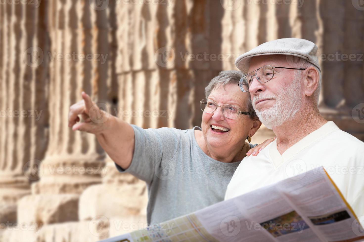 feliz pareja de adultos mayores turistas con folleto junto a las ruinas de la antigua columna. foto