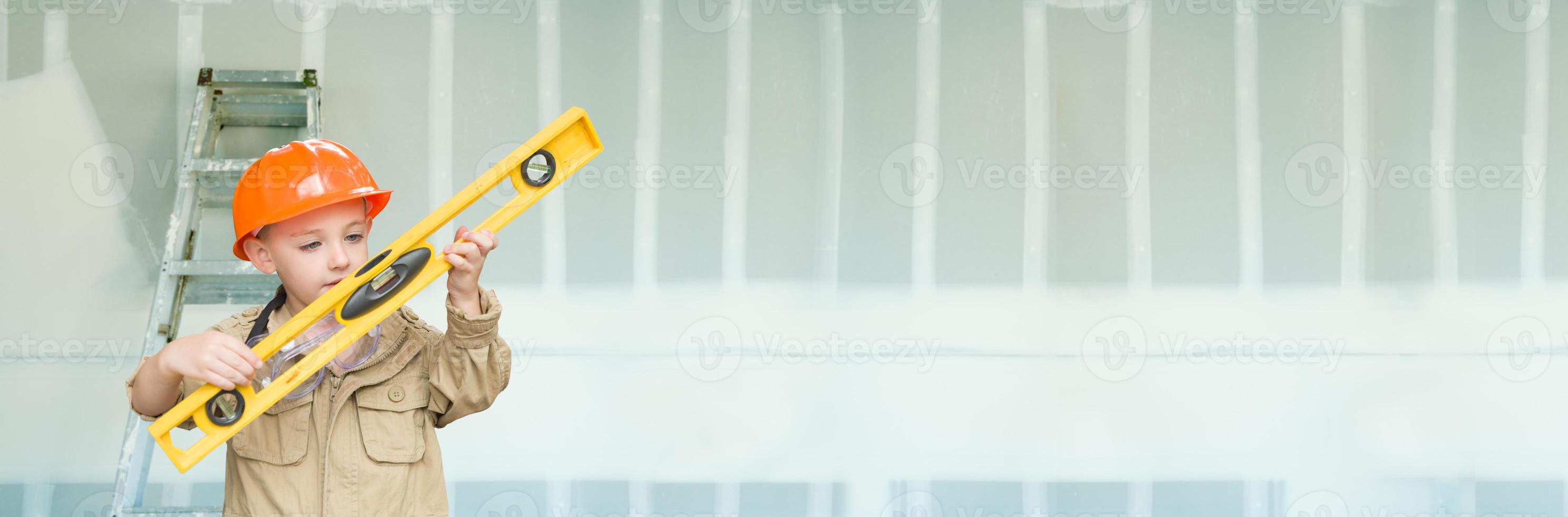 Cute Young Boy Dressed As Contractor Holding Level Against Dywall Banner Background with Ladder photo