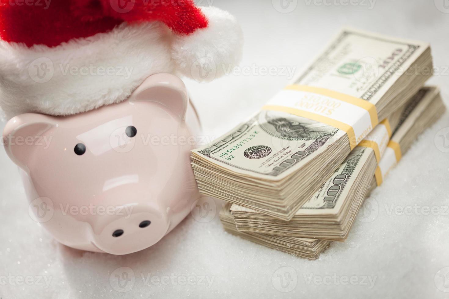 Piggy Bank Wearing Santa Hat Near Stacks of Hundred Dollar Bills on Snowflakes photo