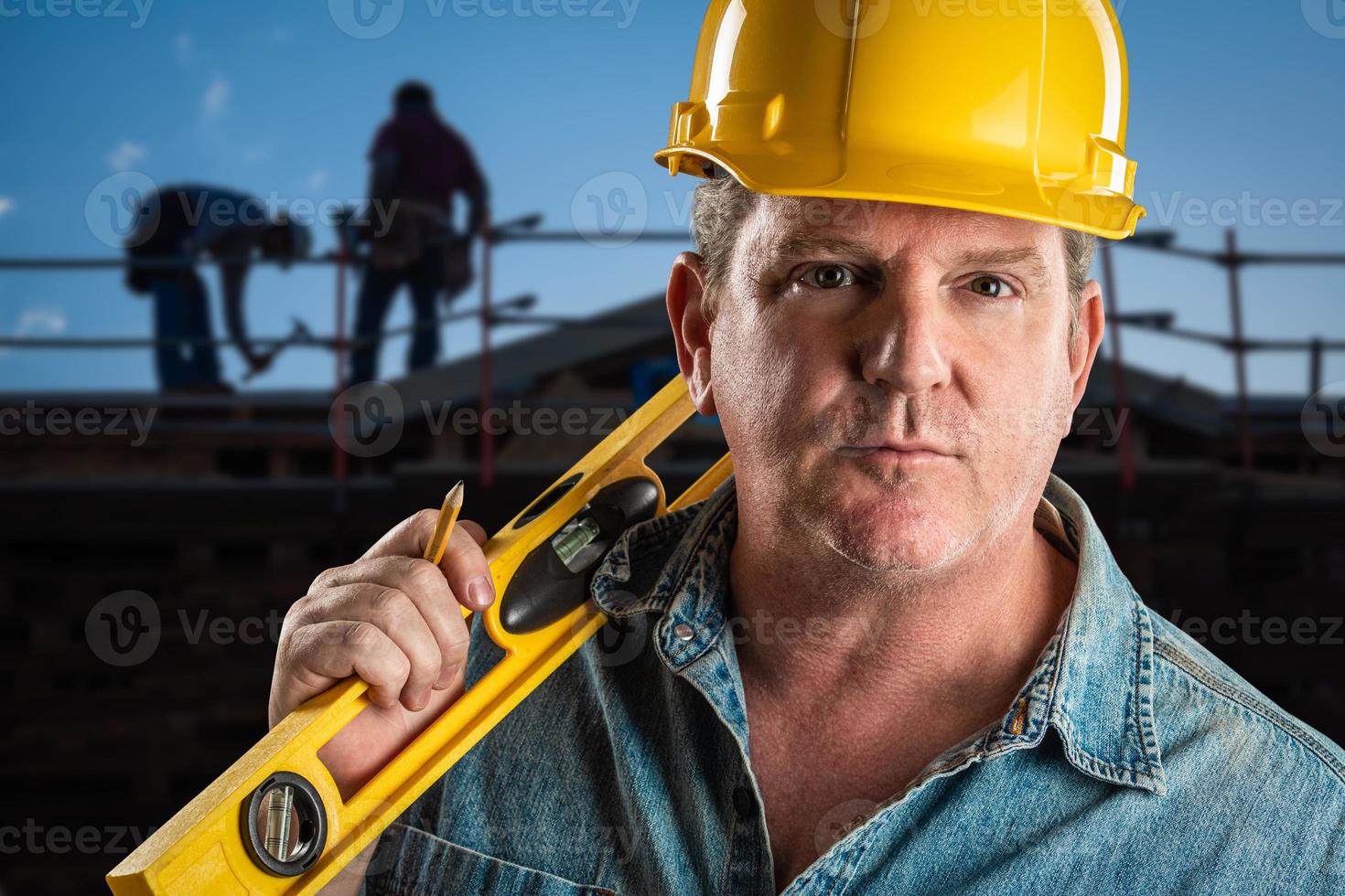 Serious Contractor in Hard Hat Holding Level and Pencil At Construction Site. photo