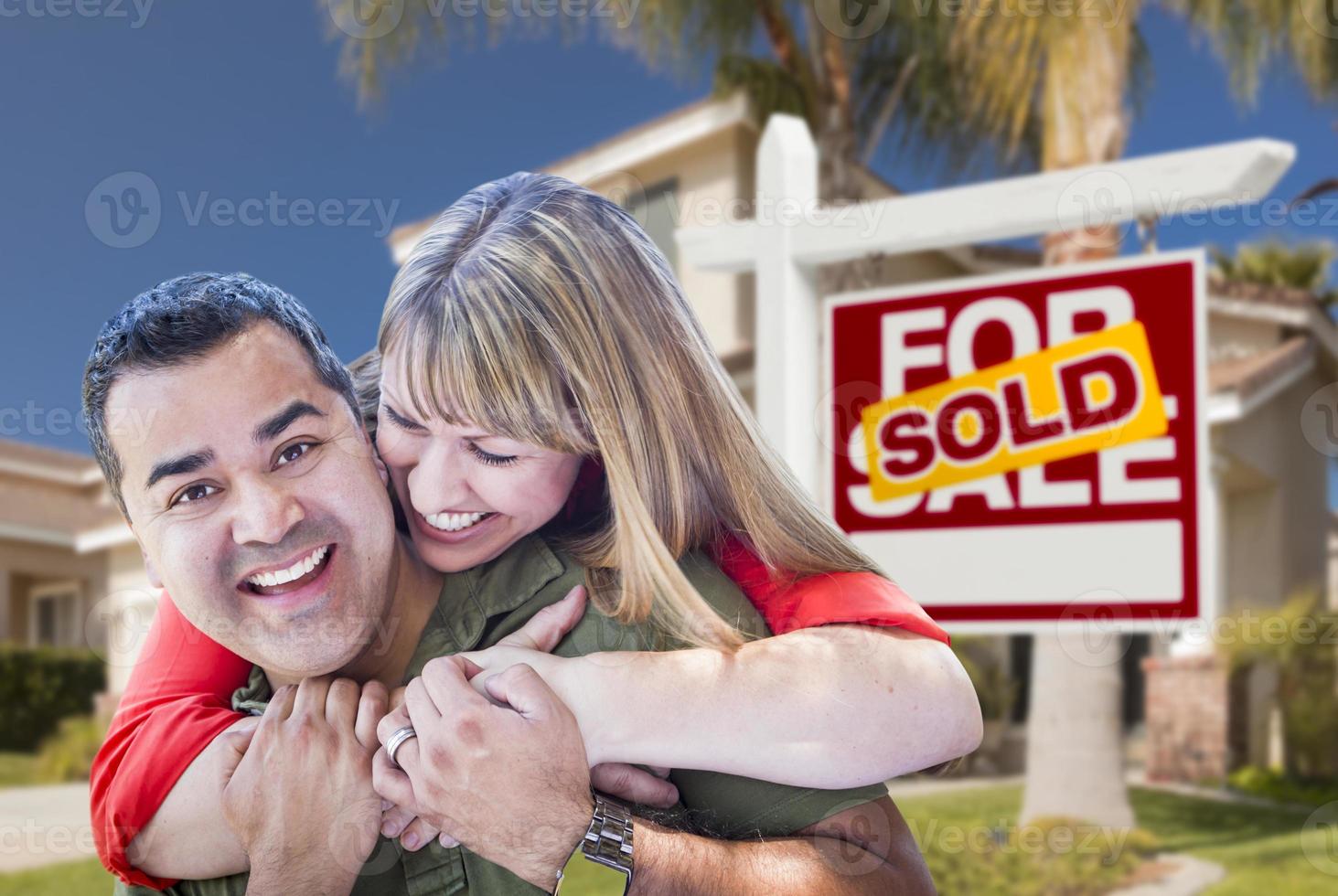 pareja frente al letrero de bienes raíces vendidos y la casa foto