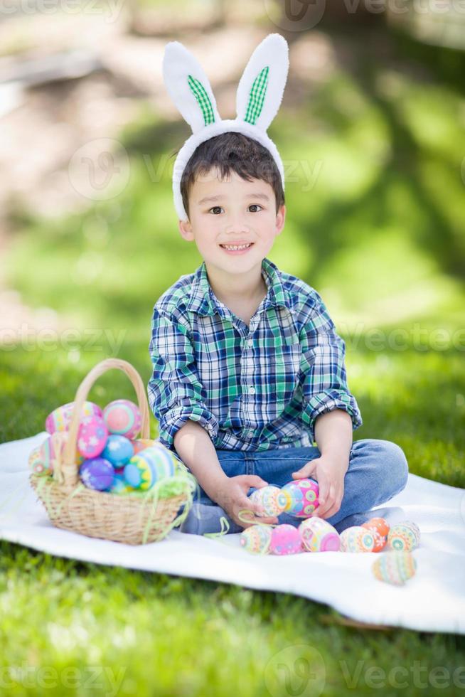 bebé de raza mixta chino y caucásico afuera usando orejas de conejo jugando con huevos de pascua foto