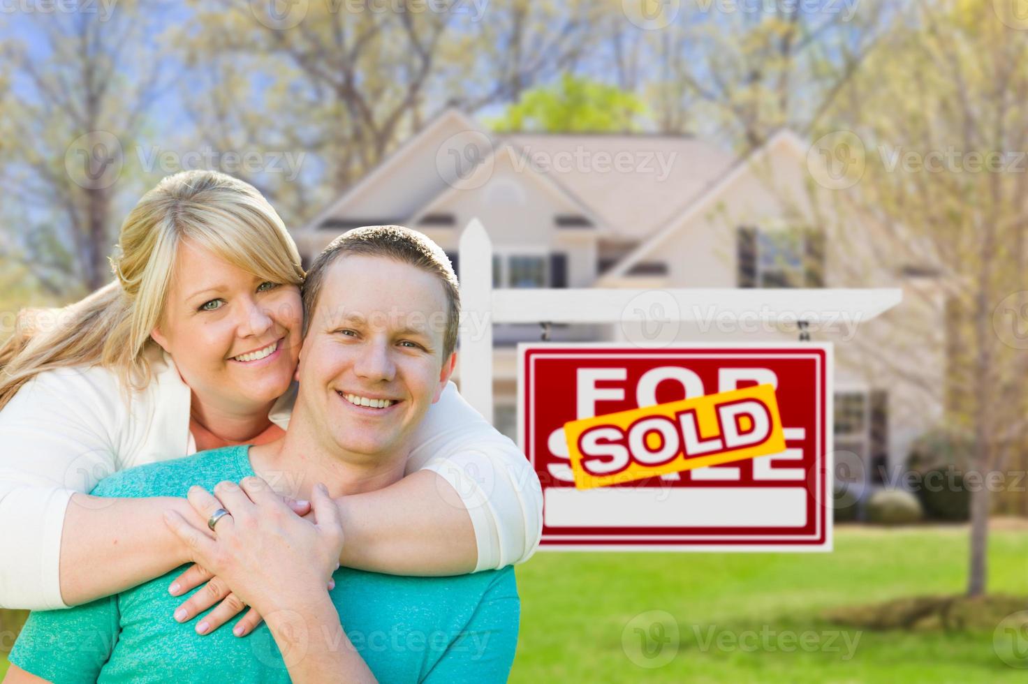 Happy Couple Hug In Front of Sold Real Estate Sign and New House photo