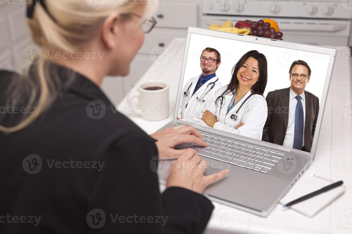 mujer en la cocina usando una laptop, en línea con enfermeras o médicos foto